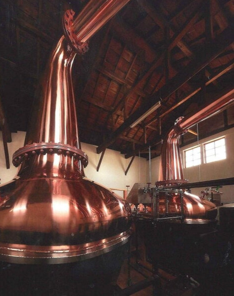 Copper pot stills and various casks used in whisky production at Aska Distillery.