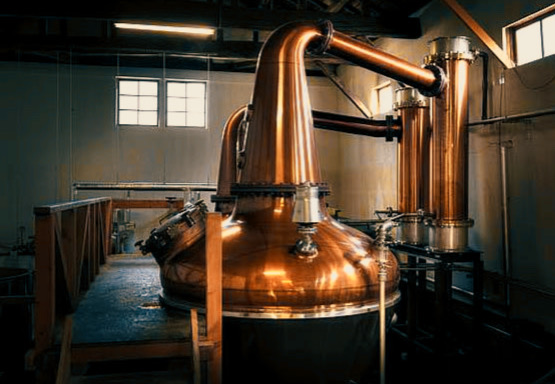 Copper pot stills and various casks used in whisky production at Aska Distillery.